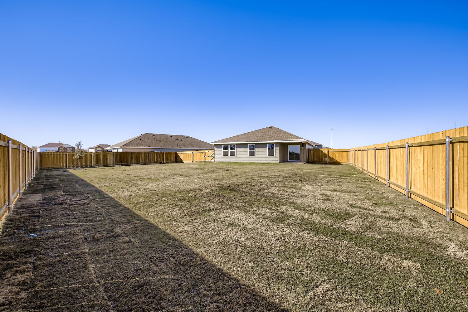 A fenced in dirt field with a building in the background.
